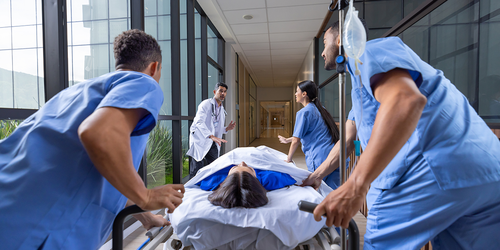 Acute care nurse checking a patient’s hand and vital monitor.