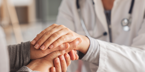 Doctor gently holding a patient’s hands in support.