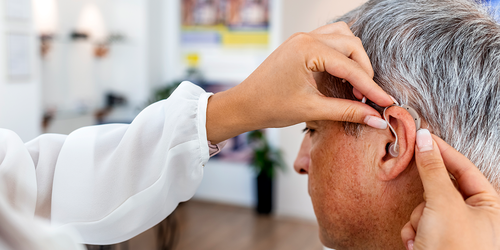 Specialist fitting a behind‑the‑ear hearing aid on an adult.