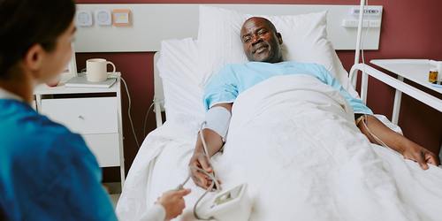 Hospitalist checking on a resting inpatient in a hospital room.