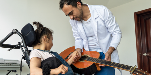 Music therapist playing guitar with child in a wheelchair.