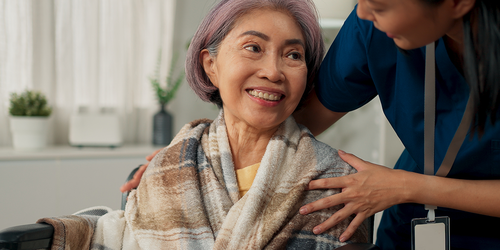 Care aide wrapping a senior patient in a warm blanket.
