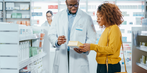 Pharmacy aide helping a customer choose an over‑the‑counter medicine.