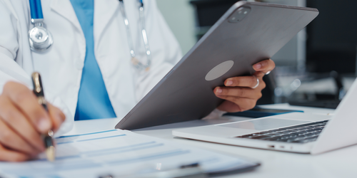 Physician using a tablet and notes during a patient consultation.