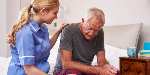 Psychiatric aide comforting an older patient sitting on a bed.