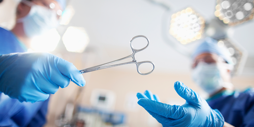 Surgical assistant passing sterile forceps to a surgeon.