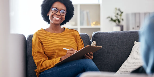 Black female therapist smiling and taking notes during a therapy session, providing professional mental health support.